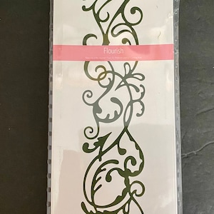 May include: A white cookie cutter die in a plastic package. The die is shaped like a 12-inch border of a flourish design. The package has the text "Cookie Cutter Dies 12" Border" and "Flourish" on it. The package also has the text "Quickutz" on it.