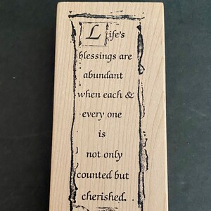 May include: A wooden stamp with a decorative border and the text "Life's blessings are abundant when each & every one is not only counted but cherished."