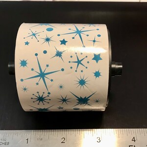 May include: A white roll of wrapping paper with a blue starburst pattern. The roll is about 3 inches in diameter.