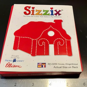 May include: A red Sizzix die-cutter for crafting, shaped like a gingerbread house with a white circle for a window. The packaging features the text "Sizzix" and "The Little Die-Cutter That Makes a Big Difference." The text "38-0234 House, Gingerbread" and "Actual Size on Back" is also visible on the packaging.