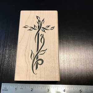 May include: A wooden stamp with a black design of a cross with leaves and vines. The stamp is approximately 2 inches wide and 3 inches tall.