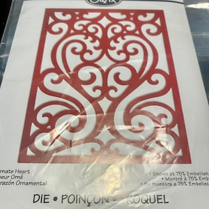May include: A red metal die cut with a decorative heart design. The die cut is shown at 75% scale. The text "DIE POINÇON ROQUEL Thinlits™" is printed on the bottom of the die cut.