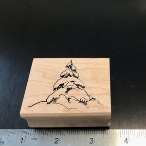 May include: A wooden rubber stamp with a black line drawing of a pine tree on a snowy background.
