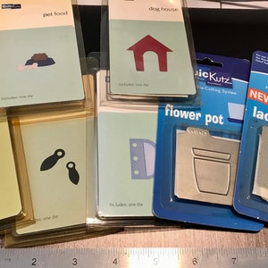 May include: Assortment of die-cutting templates for crafting, including a flower, leaves, a dog house, pet food bowl, flower pot, and lace. Each template is packaged individually and includes one die.