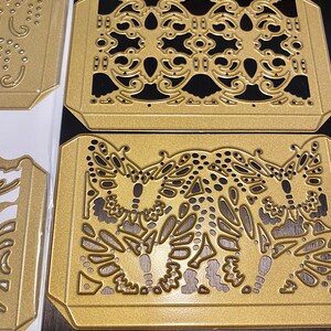 Puede incluir: Tres plantillas de metal dorado troqueladas con dise&ntilde;os intrincados. La plantilla superior presenta un patr&oacute;n repetitivo de espirales y puntos. La plantilla del medio presenta un patr&oacute;n repetitivo de espirales y puntos. La plantilla inferior presenta tres dise&ntilde;os de mariposas con espirales y puntos.