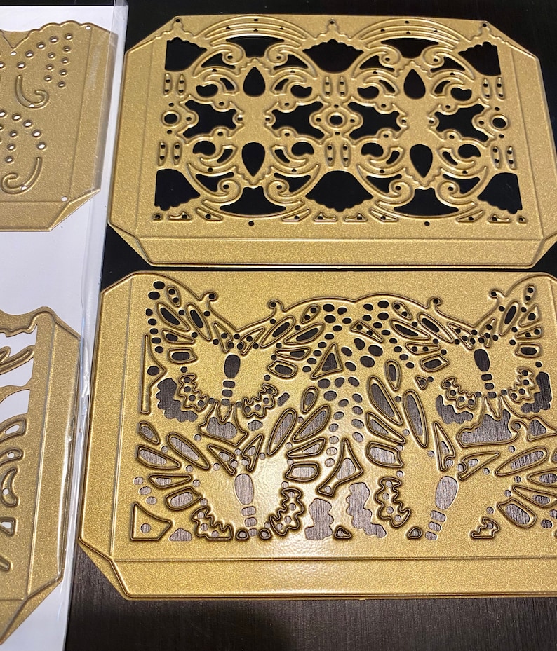 Puede incluir: Tres plantillas de metal dorado troqueladas con dise&ntilde;os intrincados. La plantilla superior presenta un patr&oacute;n repetitivo de espirales y puntos. La plantilla del medio presenta un patr&oacute;n repetitivo de espirales y puntos. La plantilla inferior presenta tres dise&ntilde;os de mariposas con espirales y puntos.