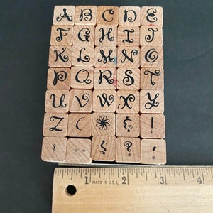 May include: A set of wooden alphabet stamps with a decorative font. The stamps are arranged in alphabetical order and include punctuation marks. The stamps are approximately 1 inch in size.