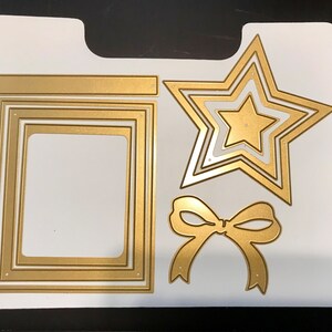 May include: A set of gold metal die-cut shapes for crafting. The set includes a star, a bow, and a frame with three layers.