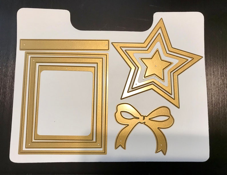May include: A set of gold metal die-cut shapes for crafting. The set includes a star, a bow, and a frame with three layers.