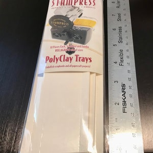 May include: A package of white PolyClay Trays for use with the Rollograph wheel system. The package includes 10 trays, in both standard and jumbo sizes. The package is labeled "STAMPRESS" and "PolyClay Trays".