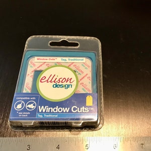May include: A clear plastic package containing a set of Ellison Design Window Cuts™ for crafting. The package is blue and white with a red and white logo. The package includes a tag that says "Window Cuts™ Tag, Traditional".