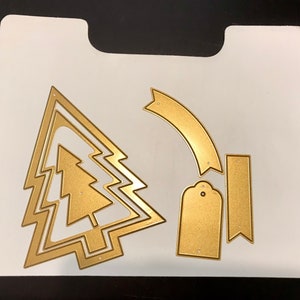 May include: A set of gold metal Christmas tree die cuts. The set includes a large tree with three layers, a smaller tree, a banner, a tag, and a rectangle.