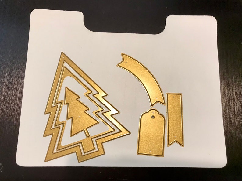 May include: A set of gold metal Christmas tree die cuts. The set includes a large tree with three layers, a smaller tree, a banner, a tag, and a rectangle.