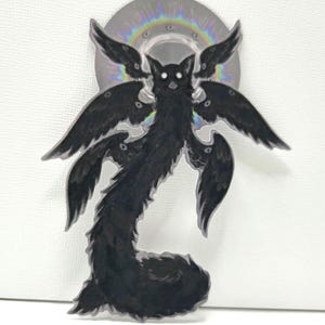 May include: A black, stylized illustration of a creature with multiple wings and a long, furry body. The creature has glowing white eyes and is set against a holographic, rainbow-colored halo. The artwork has a fantasy theme.