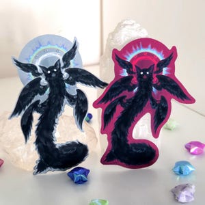 May include: Two die-cut stickers featuring a black, multi-winged creature with glowing white eyes. One sticker has a light blue holographic halo, while the other has a vibrant pink holographic halo. Both designs show a long, furry body.
