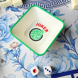 May include: A square, off-white plastic tray with a green rim, featuring the word "JOKER" in red and a green design inside a black circle. Two white dice with red and blue dots are also visible, suggesting a game theme.
