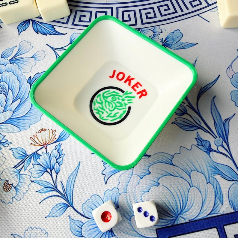 May include: A square, off-white plastic tray with a green rim, featuring the word "JOKER" in red and a green design inside a black circle. Two white dice with red and blue dots are also visible, suggesting a game theme.