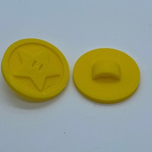 May include: Two yellow plastic buttons, one with a star-shaped design and the other with a loop on the back.