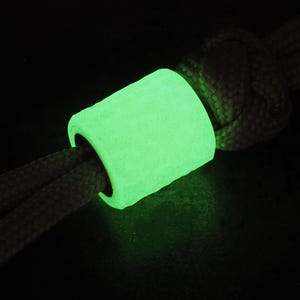 May include: A bright green glow-in-the-dark bead with a textured surface. The bead is threaded onto a grey cord.