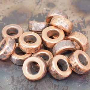 May include: A pile of copper-coloured metal beads with a hammered texture. The beads are round with a hole in the centre.