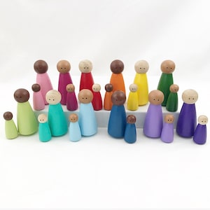Puede incluir: Un conjunto de 18 muñecas de madera con clavijas en varios colores, incluyendo verde, azul, morado, rosa, amarillo, naranja, rojo y verde claro. Las muñecas están dispuestas en un patrón de arcoíris y son de diferentes tamaños.