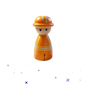 Könnte beinhalten: Eine Holzpuppe in Form eines Bauarbeiters. Die Puppe ist orange lackiert und hat silberne Reflexstreifen auf Weste und Helm. Das Gesicht ist aus unbemaltem Holz mit zwei schwarzen Punktaugen.
