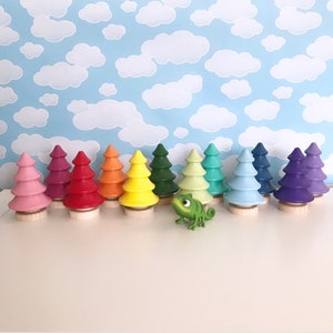 May include: A collection of colorful wooden tree figurines in various shades of pink, red, orange, yellow, green, blue, and purple. Each tree sits on a small wooden base. A green chameleon figurine is in front of the trees.