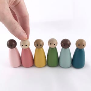 Puede incluir: Un conjunto de siete muñecos de madera, cada uno pintado de un color diferente: rosa, rosa claro, amarillo, verde, azul claro, azul y marrón. Los muñecos tienen ojos negros y están dispuestos en fila.