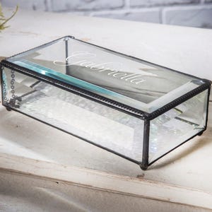 May include: A clear glass box with a black metal frame and a beaded trim. The box is engraved with the name "Gabriella".