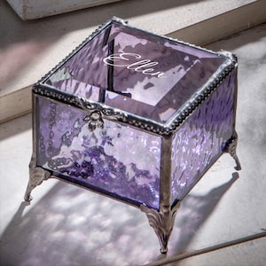 May include: A small, square, purple glass trinket box with a silver metal frame and feet. The box has a textured glass surface and is engraved with the name "Ellen".