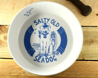 May include: White ceramic dog bowl with a blue and white illustration of a dog wearing a captain's hat and holding a fish. The text "Salty Old Seadog" is printed on the bowl.
