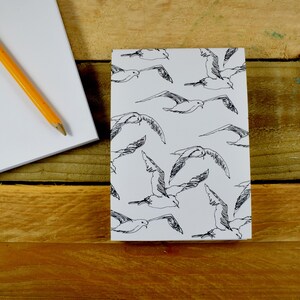 May include: A white notepad with a black and white pattern of seagulls flying in different directions. The notepad is on a wooden surface.