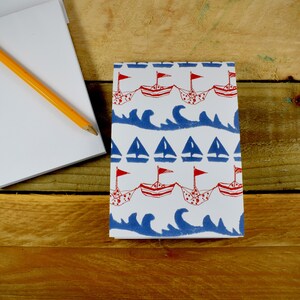 May include: A white notepad with a red, white, and blue patterned design featuring sailboats and waves. The pattern is repeated throughout the notepad.