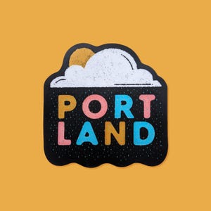 May include: Black and white sticker with a stylized cloud and sun design. The text "PORTLAND" is written in colorful letters below the cloud.