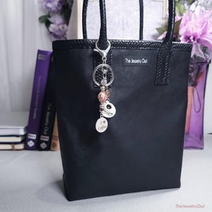May include: Black tote bag with braided handles and a silver keychain. The keychain features a coffee-themed charm with the words "I love coffee" and a panda bear charm. The bag has the text "The Jewelry Owl".
