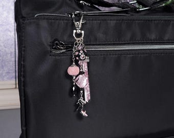 May include: A black handbag with a decorative charm. The charm features pink and black beads, a pink glitter ribbon, and a small silver high-heeled shoe. The charm is attached to a silver clasp.