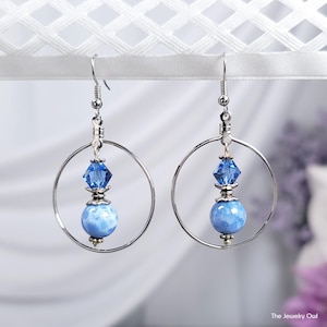 May include: A pair of silver hoop earrings with a blue agate bead and a blue crystal charm hanging from each hoop.