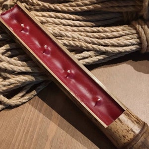 Può includere: Un portacandele rosso in bambù con quattro stoppini. Il portacandele è appoggiato su un mucchio di corda naturale.