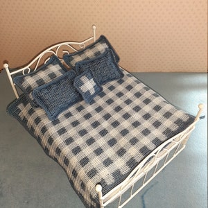 May include: A white metal doll bed frame with a blue and white checkered crocheted blanket and three blue crocheted pillows.