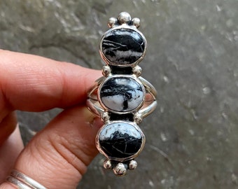 May include: A silver ring with three black and white stones set in a vertical row. The stones are round and have a natural, organic look.