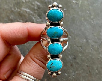 May include: A silver ring with five turquoise stones set in a vertical row. The stones are oval shaped and have a bright blue color.