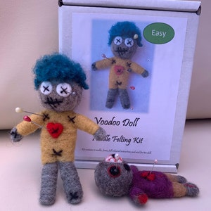Könnte beinhalten: Ein Nadelfilz-Set zum Herstellen von zwei Voodoo-Puppen. Das Set enthält zwei Nadeln, Wolle und Anleitungen. Die Puppen sind mit blauen Haaren, gelben Hemden und roten Herzen dargestellt. Die Puppen sind mit Nadeln befestigt. Die Schachtel ist mit "Voodoo Doll Needle Felting Kit" und "Einfach" beschriftet.