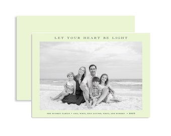 May include: A light green card with a family photo on the front. The black and white photo shows a family of five sitting on a beach. The text "LET YOUR HEART BE LIGHT" is above the photo. The text "THE HUSKET FAMILY • ANN, WHIT, ANN LOUISE, WHIT, AND ROBERT • 2025" is below the photo.