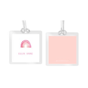 May include: Two white luggage tags with a pink watercolor rainbow design. The left tag has the name "ELLIS ANNE" printed below the rainbow. The right tag has the text "@sweetheartdesigns" printed in small font at the bottom.