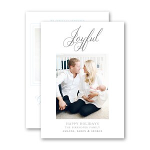 May include: A white holiday card with the word "Joyful" in cursive script. The card features a family photo of a couple and a baby. The text "Happy Holidays" and family names are printed at the bottom.