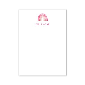 Puede incluir: Papelería blanca con un diseño de arcoíris en acuarela en tonos rosas y rojos. El nombre "ELLIS ANNE" está impreso en rosa debajo del arcoíris. La papelería es rectangular.