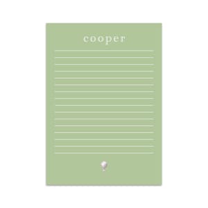 Puede incluir: Un bloc de notas verde con líneas y el nombre "cooper" impreso en la parte superior. Un tee de golf blanco con una bola de golf blanca en la parte superior se encuentra en la parte inferior del bloc de notas.