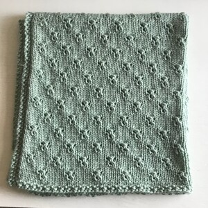 May include: A soft, sage green knitted baby blanket with a diamond pattern.