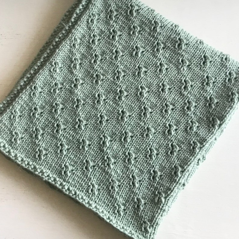 May include: A soft, sage green knitted baby blanket with a delicate diamond pattern.