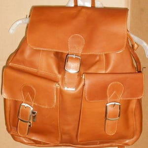 Pu&ograve; includere: Uno zaino in pelle marrone con due grandi tasche anteriori e due fibbie. Lo zaino ha una patta con chiusura a fibbia.